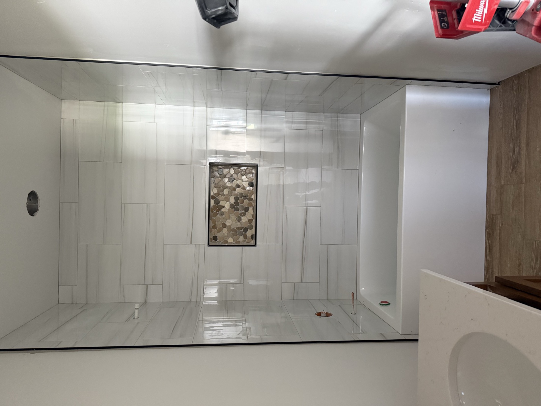Custom shower with stacked white tile and pebble accent niche
