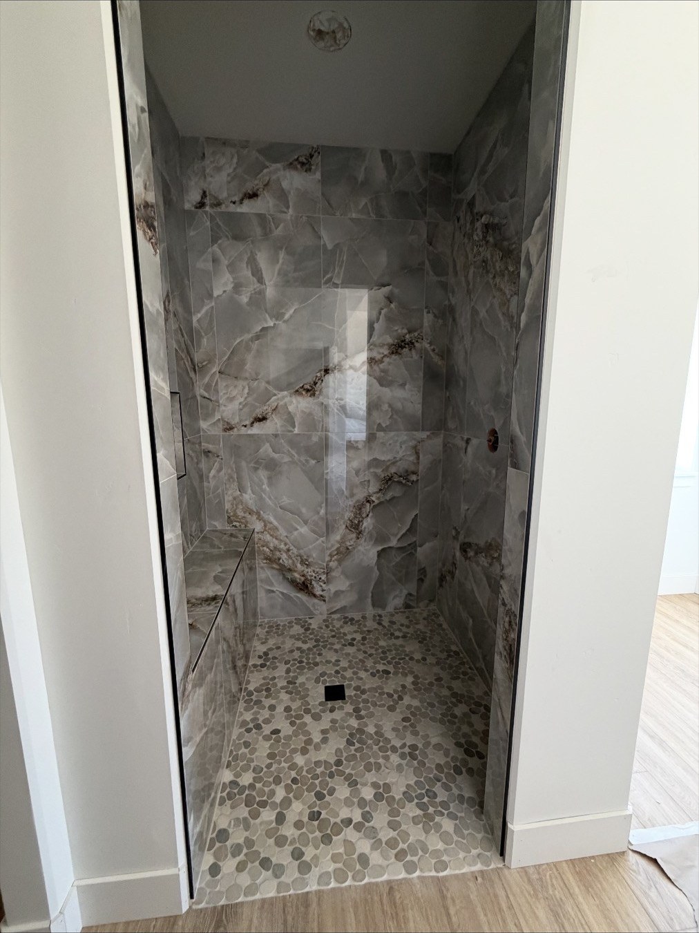 Walk-in shower with floor-to-ceiling marble tile and pebble floor